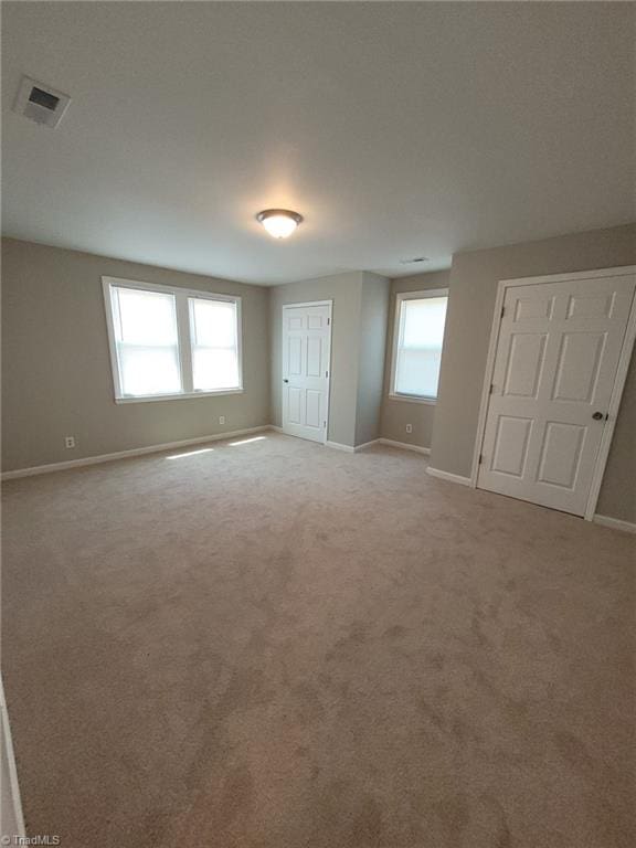unfurnished bedroom with baseboards, visible vents, multiple windows, and light carpet