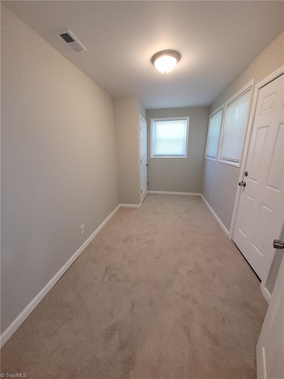 empty room featuring baseboards, visible vents, and light colored carpet