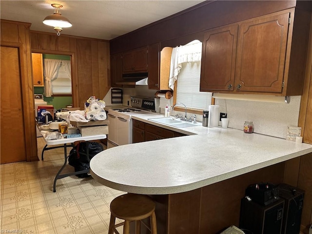 kitchen featuring white electric range oven, a kitchen breakfast bar, kitchen peninsula, and sink