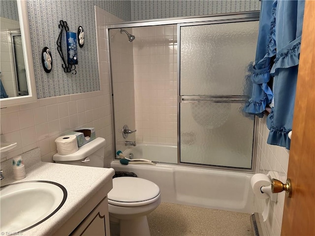 full bathroom featuring combined bath / shower with glass door, vanity, toilet, and tile walls