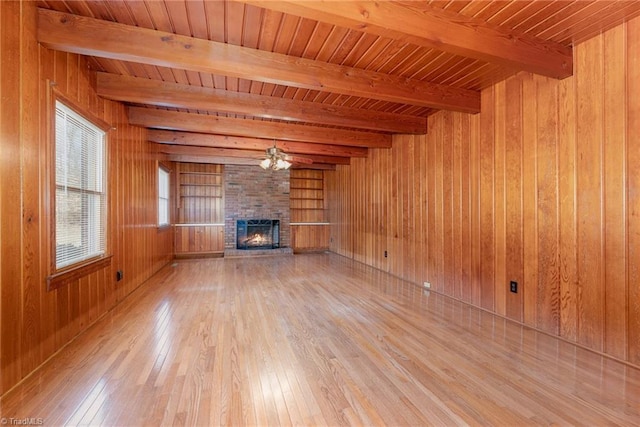 unfurnished living room with light wood-type flooring, a brick fireplace, wooden walls, and beamed ceiling