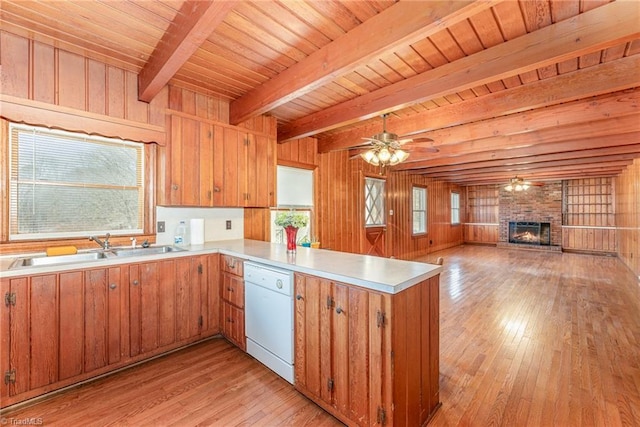 kitchen with light hardwood / wood-style flooring, wooden walls, white dishwasher, a brick fireplace, and kitchen peninsula