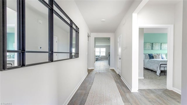 corridor featuring light wood-type flooring and baseboards