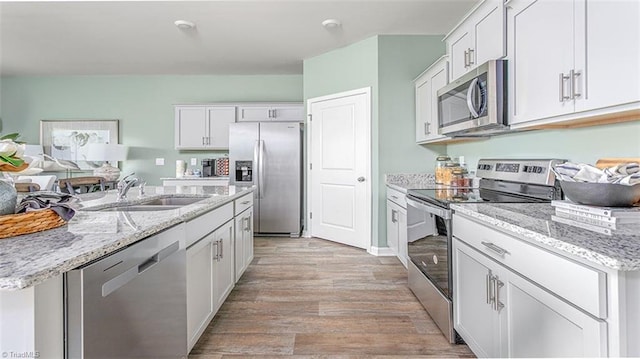 kitchen featuring white cabinets, light wood-style flooring, appliances with stainless steel finishes, open floor plan, and a sink