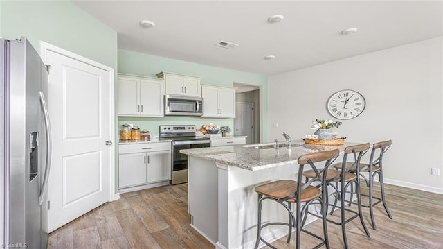 kitchen with a breakfast bar area, a sink, white cabinets, appliances with stainless steel finishes, and a center island with sink