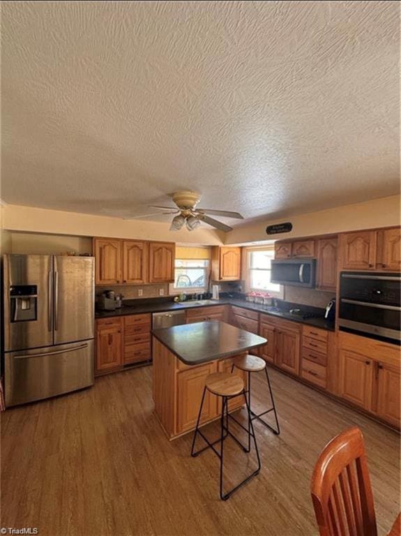 357 Town N Country Dr, Wilkesboro, NC 28697 - kitchen with stainless steel appliances, a textured ceiling, wood finished floors, brown cabinetry, and dark countertops