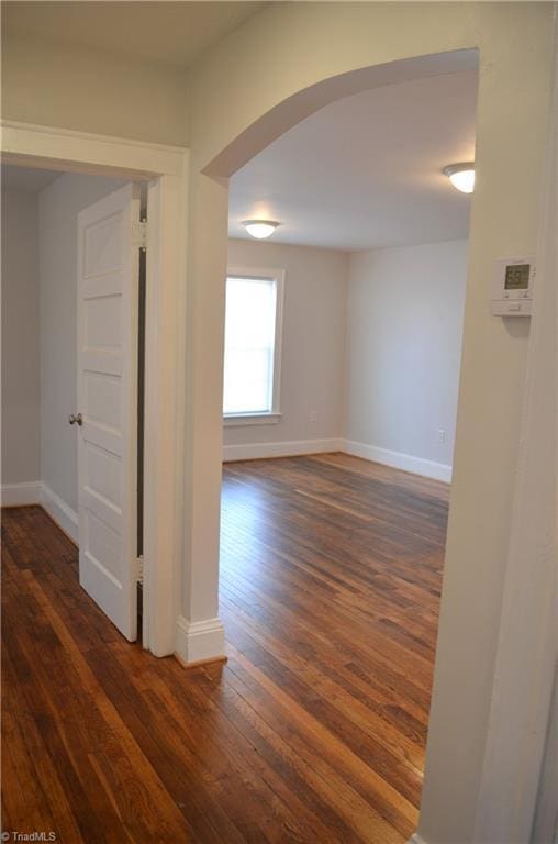 spare room with baseboards, arched walkways, and dark wood finished floors
