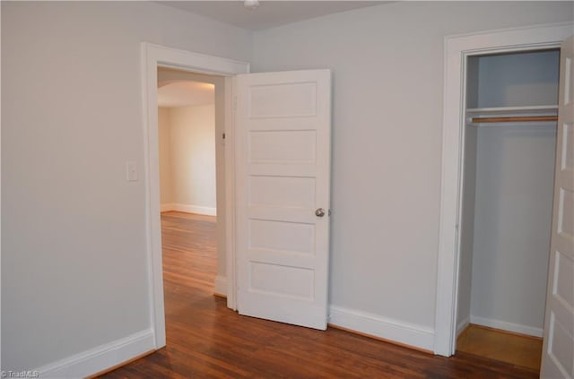 unfurnished bedroom featuring arched walkways, dark wood-style floors, a closet, and baseboards