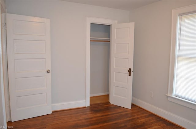 unfurnished bedroom with a closet, baseboards, and dark wood finished floors