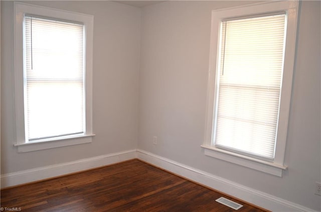 unfurnished room featuring dark wood-style flooring, visible vents, and baseboards