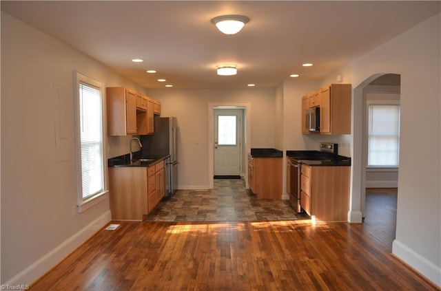 kitchen featuring baseboards, arched walkways, dark wood-style flooring, dark countertops, and stainless steel appliances