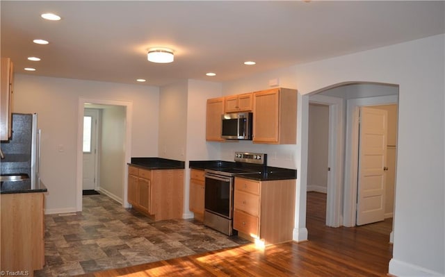 kitchen featuring dark countertops, appliances with stainless steel finishes, arched walkways, and recessed lighting