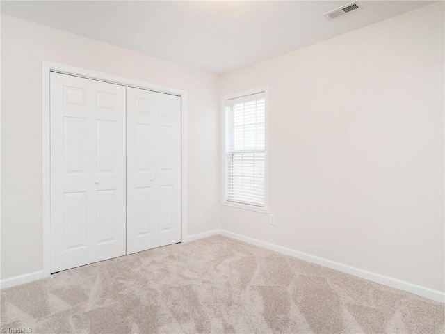 unfurnished bedroom with light colored carpet and a closet