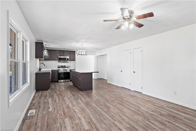 kitchen featuring a kitchen island, appliances with stainless steel finishes, hardwood / wood-style floors, decorative light fixtures, and sink