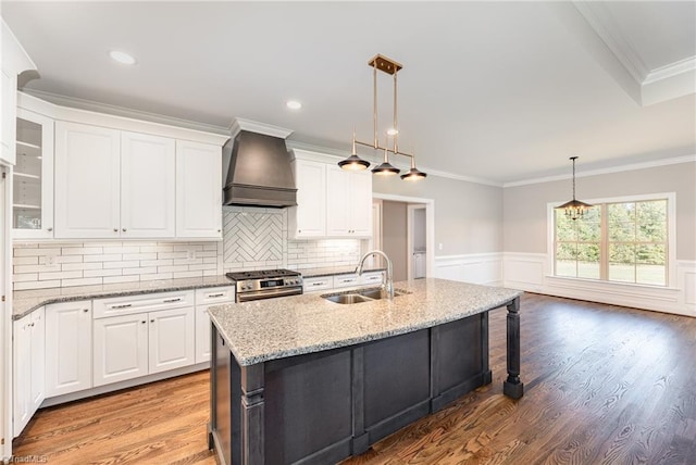 kitchen with a kitchen island with sink, stainless steel range with gas cooktop, custom exhaust hood, and white cabinets