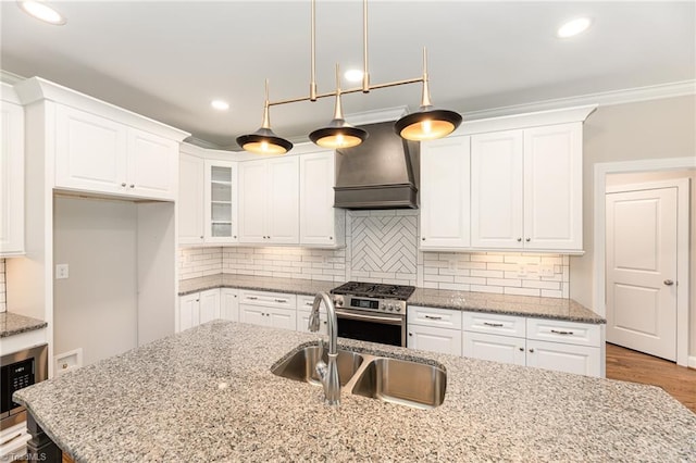 kitchen featuring stainless steel gas stove, decorative light fixtures, sink, white cabinets, and custom range hood