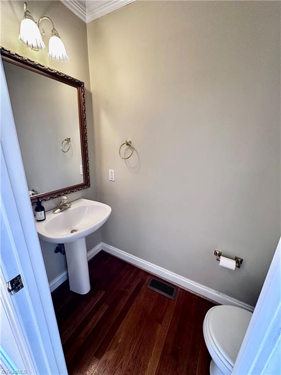 half bath with visible vents, baseboards, toilet, and wood finished floors