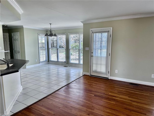 interior space featuring crown molding, baseboards, light wood-style flooring, an inviting chandelier, and a sink