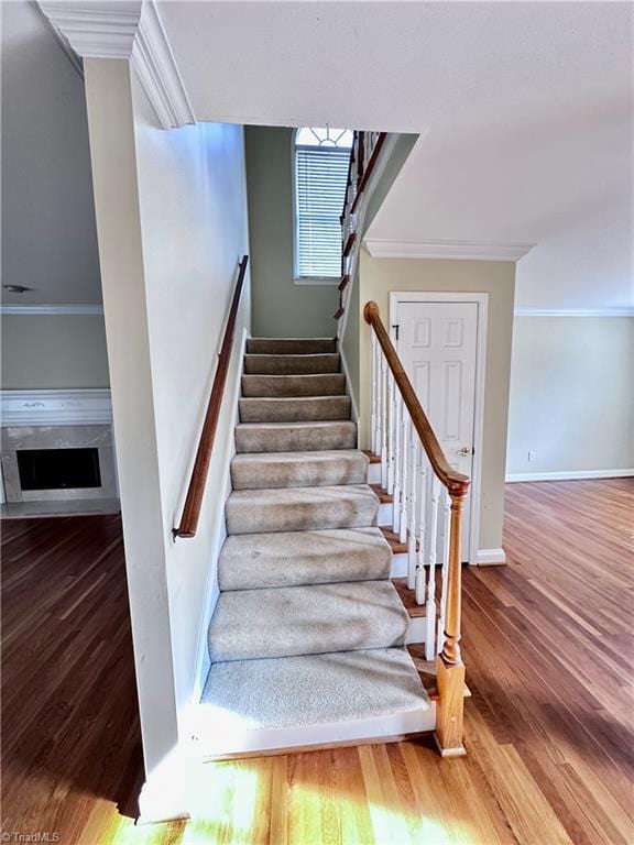 staircase with a fireplace, wood finished floors, baseboards, and ornamental molding