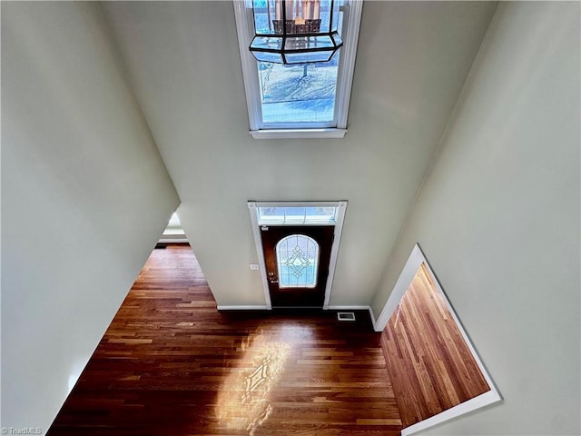 entrance foyer featuring visible vents, baseboards, wood finished floors, and a towering ceiling