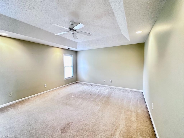 empty room with a tray ceiling, baseboards, a textured ceiling, and ceiling fan