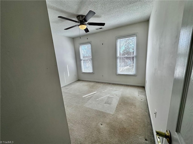 carpeted spare room with baseboards, visible vents, a textured ceiling, and a ceiling fan