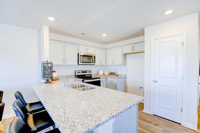 kitchen featuring kitchen peninsula, light stone counters, a breakfast bar, stainless steel appliances, and light hardwood / wood-style flooring