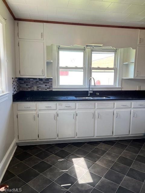 kitchen with dark tile patterned flooring, sink, backsplash, white cabinetry, and crown molding