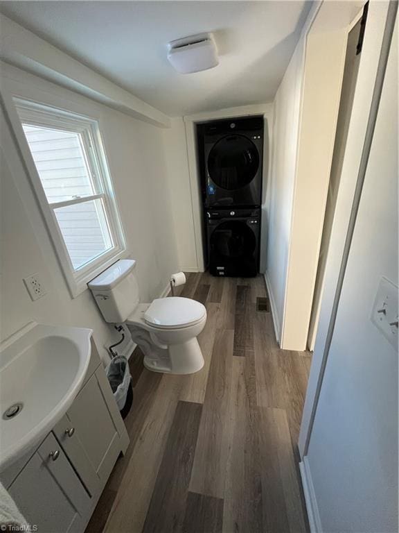 bathroom with hardwood / wood-style floors, vanity, toilet, and stacked washer and dryer