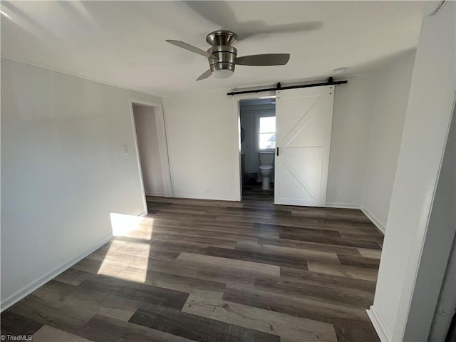 unfurnished room featuring a barn door, dark hardwood / wood-style floors, and ceiling fan