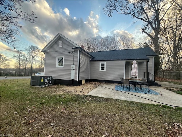 back house at dusk with cooling unit, a patio area, and a lawn