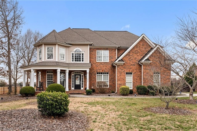 view of front facade with a front lawn, fence, brick siding, and roof with shingles