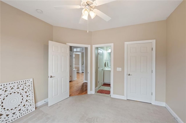 unfurnished bedroom with light colored carpet, ensuite bath, baseboards, and ceiling fan