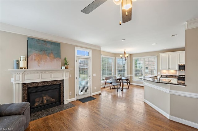 living area with a high end fireplace, crown molding, baseboards, ceiling fan with notable chandelier, and wood finished floors