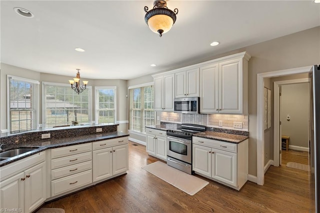 kitchen with dark wood finished floors, decorative backsplash, appliances with stainless steel finishes, white cabinets, and a sink