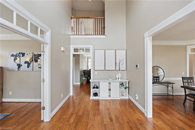 corridor featuring baseboards, a high ceiling, wood finished floors, and ornamental molding