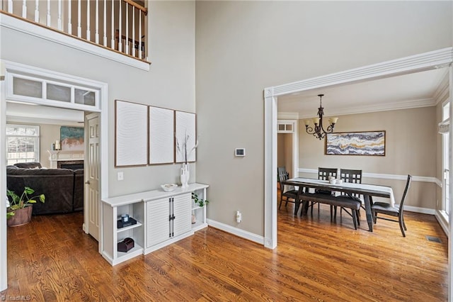 interior space with ornamental molding, wood finished floors, an inviting chandelier, a fireplace, and baseboards