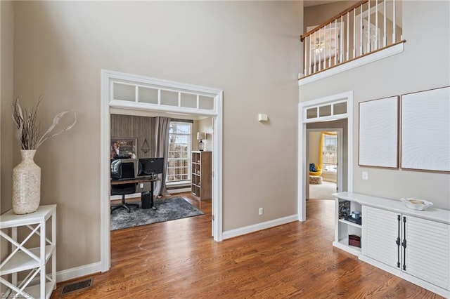 interior space featuring visible vents, a towering ceiling, baseboards, and wood finished floors