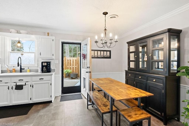 kitchen with pendant lighting, white cabinetry, sink, ornamental molding, and a notable chandelier