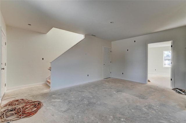 unfurnished living room featuring stairway and baseboards