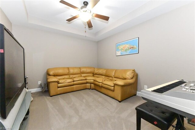 living area with a raised ceiling, a ceiling fan, baseboards, and carpet