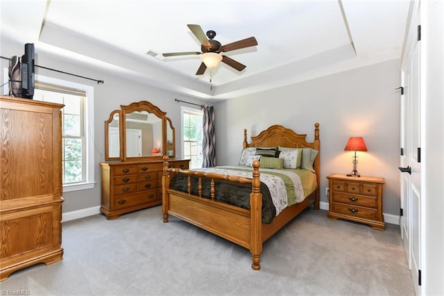 bedroom with a ceiling fan, a tray ceiling, light carpet, and baseboards