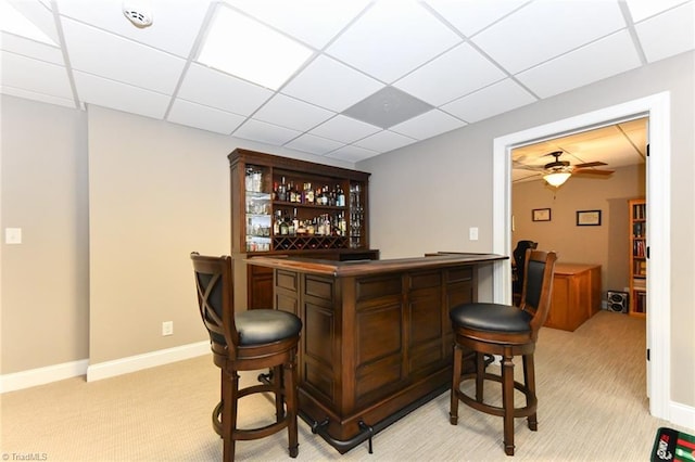 bar featuring baseboards, a bar, a paneled ceiling, and light carpet