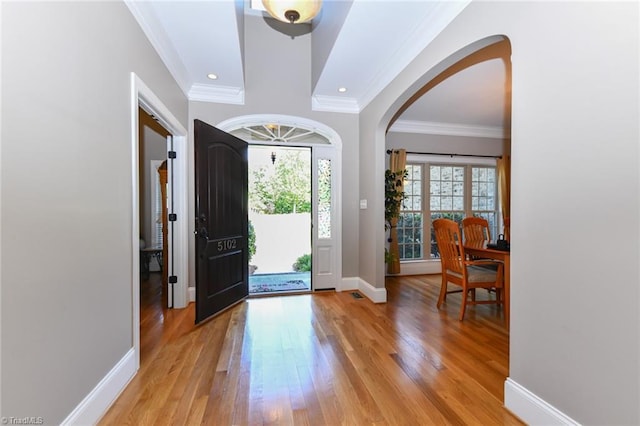 entrance foyer with light wood-type flooring, arched walkways, and ornamental molding