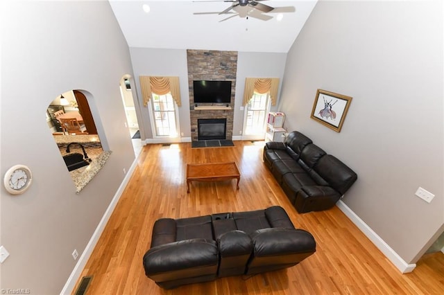 living area with arched walkways, ceiling fan, baseboards, and high vaulted ceiling