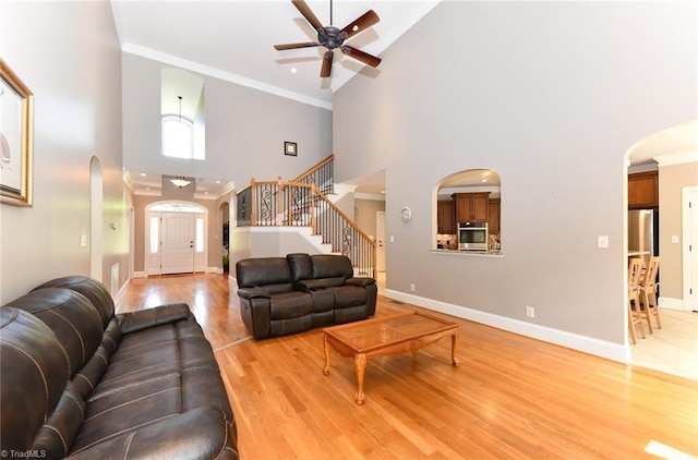 living area with ceiling fan, arched walkways, stairway, high vaulted ceiling, and light wood finished floors