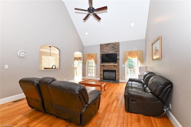 living area with ceiling fan, a stone fireplace, high vaulted ceiling, baseboards, and light wood finished floors