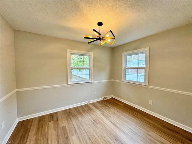 spare room featuring a chandelier, wood-type flooring, a textured ceiling, and a wealth of natural light