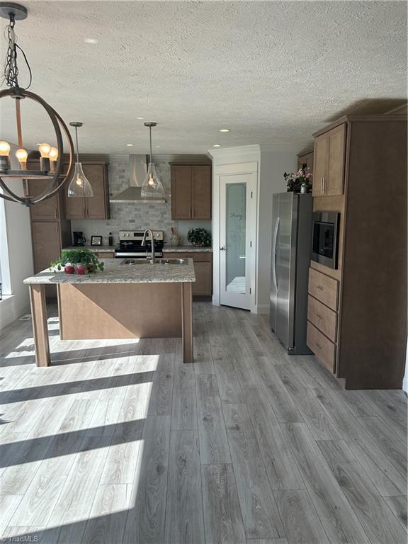 3700 Ireland Rd, Yadkinville, NC 27011 - kitchen featuring appliances with stainless steel finishes, wall chimney range hood, a chandelier, light wood-style floors, and a textured ceiling