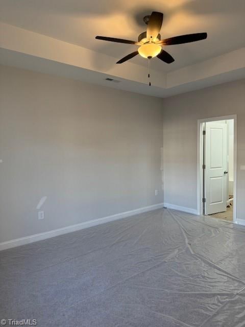 empty room featuring ceiling fan, a raised ceiling, and carpet flooring